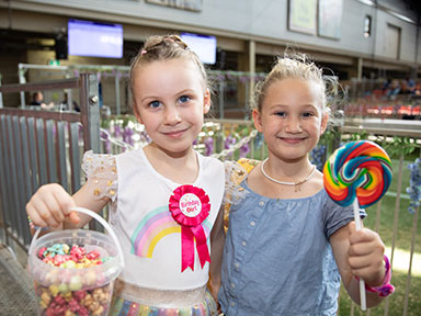 Two children smile holding sweets and a large rainbow lollipop at the Sydney Royal Easter Show.