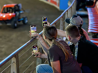 A group of spectators in reserved seats film cars in motion on their mobile phones at the Sydney Royal Easter Show.